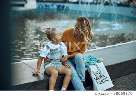 Excited girl sitting with mother on the fountain stock photo Excited girl sitting with mother on the fountain stock photo 58069370