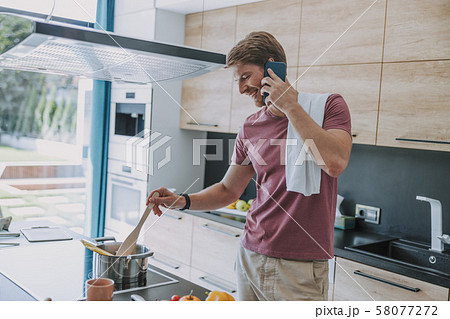 Cheerful man cooking dinner and talking to a friend 58077272