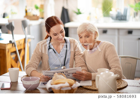 Caregiver reading morning news for retired woman 58081693