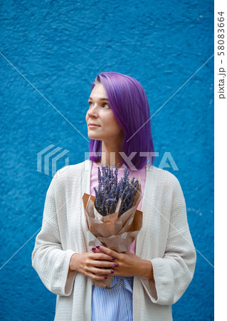 Purple haired woman in white cardigan holding a lavender bouquet in her hands. 58083664