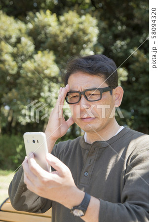 代々木公園でスマホの画面を見ながら考え込むシニア男性 代々木公園でスマホの画面を見ながら考え込むシニア男性 58094320