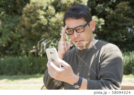 代々木公園でスマホの画面を見ながら考え込むシニア男性 代々木公園でスマホの画面を見ながら考え込むシニア男性 58094324