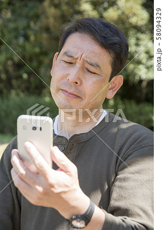 代々木公園でスマホの画面を見ながら考え込むシニア男性 代々木公園でスマホの画面を見ながら考え込むシニア男性 58094329
