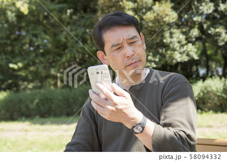 代々木公園でスマホの画面を見ながら考え込むシニア男性 58094332