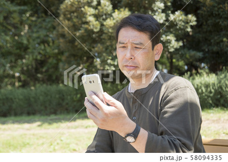 代々木公園でスマホの画面を見ながら考え込むシニア男性 58094335