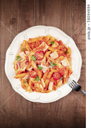 Penne pasta with chicken, tomato sauce and parsley, shot from the top on a dark rustic wooden Penne pasta with chicken, tomato sauce and parsley, shot from the top on a dark rustic wooden 58094694