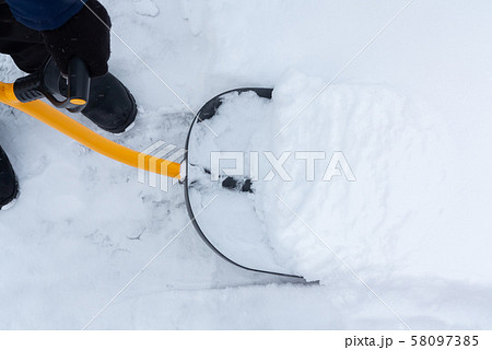 A man cleans snow in the yard with a shovel after a heavy snowfall A man cleans snow in the yard with a shovel after a heavy snowfall 58097385