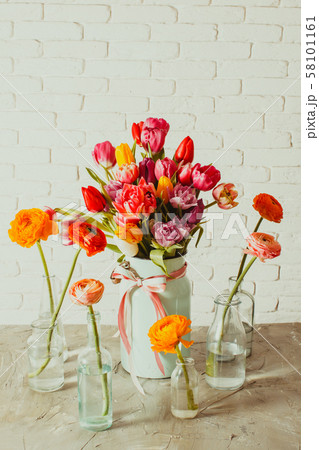 Glass bottles with ranunculus flowers around vase with tulips 58101161