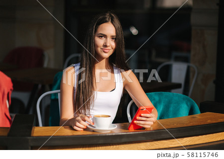Attractive young woman using phone in the cafe. Beautiful brunette girl chatting Attractive young woman using phone in the cafe. Beautiful brunette girl chatting 58115746