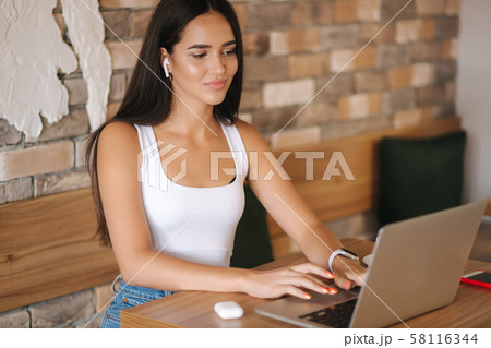 Attractive young girl use wirreless headphones and workin on her laptop. Woman in white t-shirt and 58116344