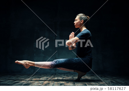 Young beautiful woman doing yoga asana tiptoe pose prapadasana variation on dark room 58117627
