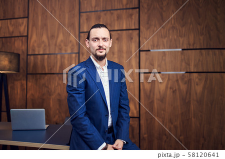 Photo of young man standing near table with laptop on background of wooden wall . Photo of young man standing near table with laptop on background of wooden wall . 58120641