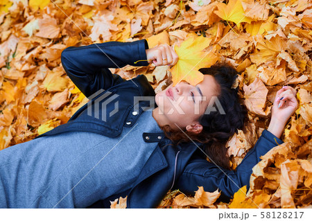 woman lying with autumn leaves in city park, 58128217