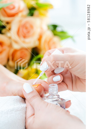 Pedicurist applying white color to foot nails of woman Pedicurist applying white color to foot nails of woman 58128982