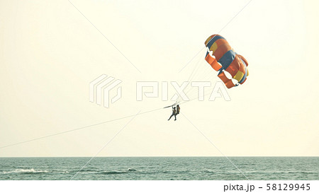 Couple flying with parachute over sea on summer day. 58129945