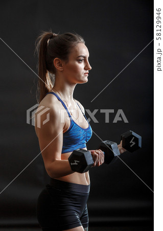 A young sport lady with ponytail in fitness clothes training with dumbells 58129946