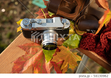 Autumn mood still life: vintage rangefinder camera, brown leather holster, red scarf and leaves laying on wooden railings Autumn mood still life: vintage rangefinder camera, brown leather holster, red scarf and leaves laying on wooden railings 58130962