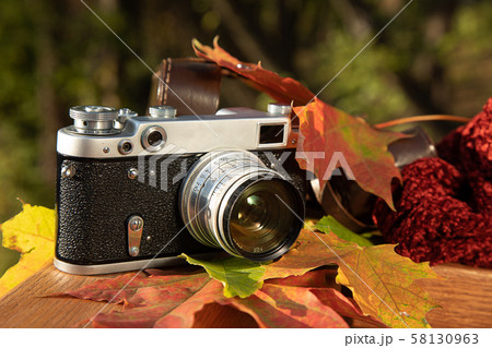Autumn mood still life: vintage rangefinder camera, brown leather holster, red scarf and leaves laying on wooden railings Autumn mood still life: vintage rangefinder camera, brown leather holster, red scarf and leaves laying on wooden railings 58130963