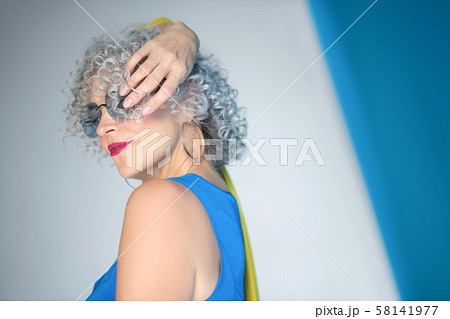 Mature curly photo model with bright lips posing near wall 58141977