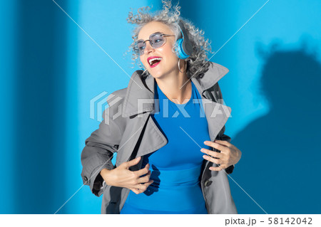 Woman wearing grey coat laughing while listening to earphones Woman wearing grey coat laughing while listening to earphones 58142042