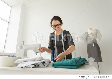 Dressmaker, fashion designer, tailor and people concept - Portrait of a seamstress at work in her Dressmaker, fashion designer, tailor and people concept - Portrait of a seamstress at work in her 58148637