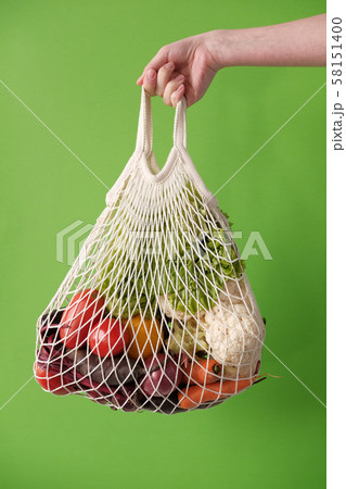 Female hand holding string eco bag with vegetables 58151400