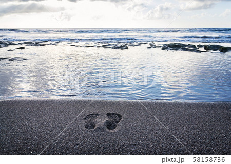 Human barefoot footprints in sand heading to sea awaiting incoming wave, sunny cloudy sunrise Human barefoot footprints in sand heading to sea awaiting incoming wave, sunny cloudy sunrise 58158736