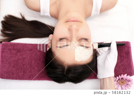 Young girl is enjoying facial procedure at beauty salon. She is lying and getting clay mask with 58162132