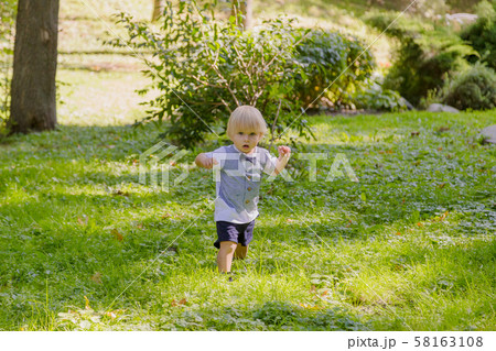 Happy little boy on a green lawn in a park. 58163108