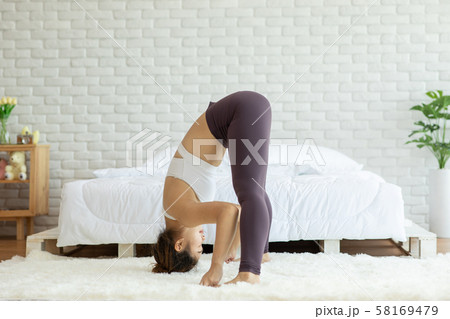 Athletic Asian woman practice yoga Spread foot stretching pose or Prasarita Padottanasana pose to meditation in bedroom after wake up in the morning Feeling so comfortable and relax,Healthcare Concept 58169479