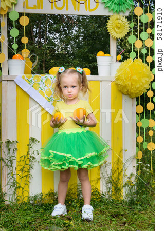 Little girl with orange near lemonade stand in Little girl with orange near lemonade stand in 58171910