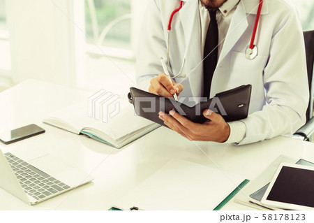 Doctor reading while writing note on a book. 58178123