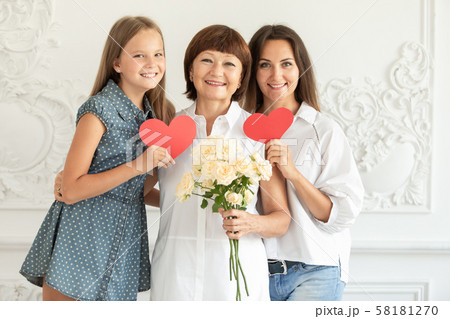 Mother, daughter and granddaughter hug and hold cardboard hearts and a bouquet of flowers Mother, daughter and granddaughter hug and hold cardboard hearts and a bouquet of flowers 58181270