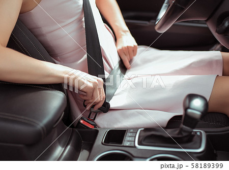A woman in car interior, fastens her seat belt, pink dress, automatic gearbox, close-up, safety 58189399