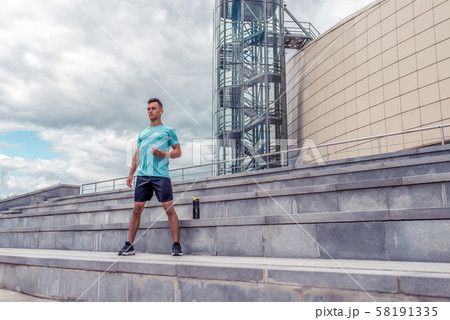 Male athlete in summer city listens to music with headphones, mobile phone, timer, time training 58191335