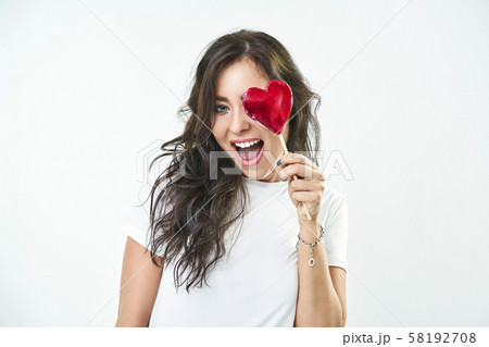 Portrait of a cute girl with a heart shaped lollipop. Woman smiling, looking at the camera Portrait of a cute girl with a heart shaped lollipop. Woman smiling, looking at the camera 58192708