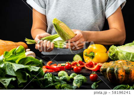Woman peeling a corn cob, cooking different vegetables. Healthy vegetarian food concept. 58196241