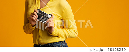 Unrecognizable millennial girl holding retro camera on yellow background, cropped Unrecognizable millennial girl holding retro camera on yellow background, cropped 58198259