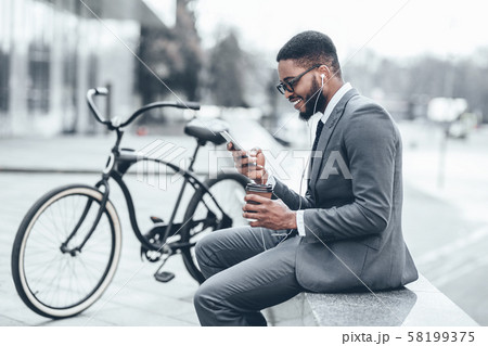 African-american businessman using phone outdoors with bike nearby 58199375