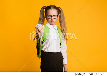 Discontented Schoolgirl Gesturing Thumbs Down Over Yellow Background Discontented Schoolgirl Gesturing Thumbs Down Over Yellow Background 58199573