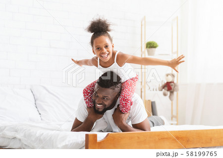 Cheerful african girl playing with father, flying like plane 58199765