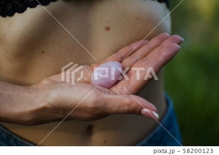 Adult woman is holding pink quartz yoni egg for vumfit, imbuilding or meditation outdoors over her Adult woman is holding pink quartz yoni egg for vumfit, imbuilding or meditation outdoors over her 58200123