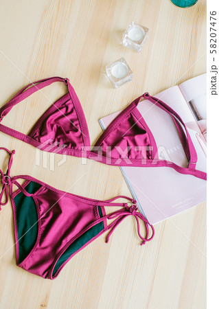 Bright trendy bikinis on a wooden background and fashion magazines. Fashionable beachwear and accessories. Bright trendy bikinis on a wooden background and fashion magazines. Fashionable beachwear and accessories. 58207476