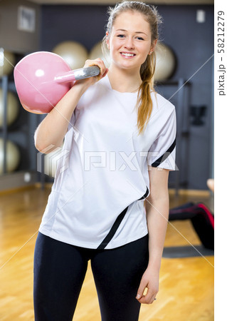 Smiling woman in workout outfit holds kettlebell at fitness gym Smiling woman in workout outfit holds kettlebell at fitness gym 58212279