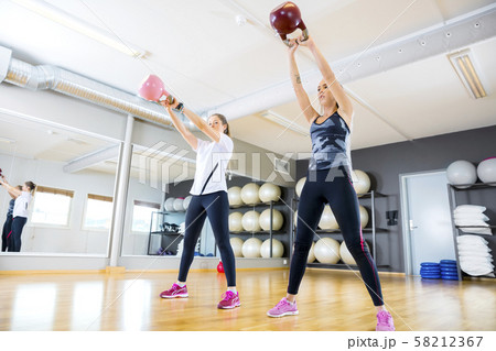 Two women trains with kettlebells at fitness gym 58212367