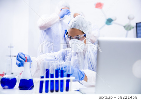 Woman chemist who works at the table and has two colleagues behind her Woman chemist who works at the table and has two colleagues behind her 58221458