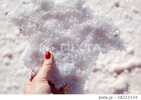 Female hand holding natural salt crystals on the background of a salt lake, side view close up Female hand holding natural salt crystals on the background of a salt lake, side view close up 58221534