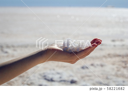 Female hand holding natural salt crystals on the background of a salt lake, side view 58221682