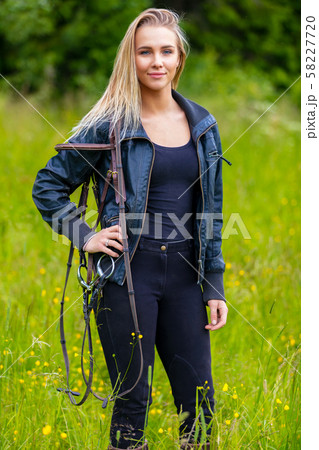 Beautilful young female horse rider standing in a green meadow 58227720