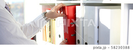 Male arms pick red file folder from office book shelf Male arms pick red file folder from office book shelf 58230388